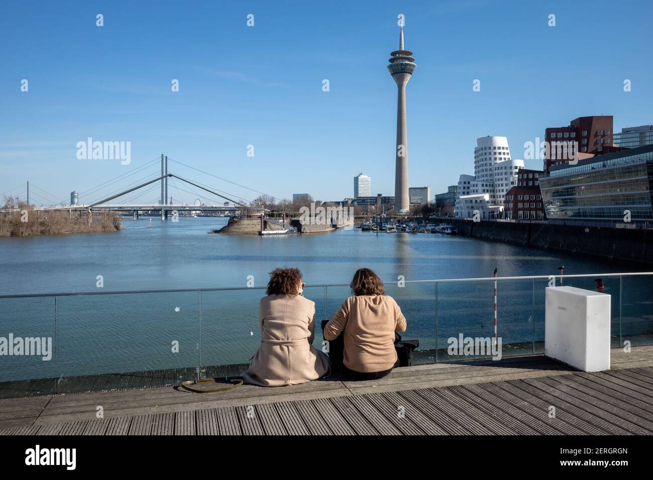Frauen sitzen auf Brücke im Medienhafen, Fußgängerbrücke am Medienhafen und im Hintergrund Hafen, Rheinturm, Neuer Zollhof und Promenade. Stockfoto