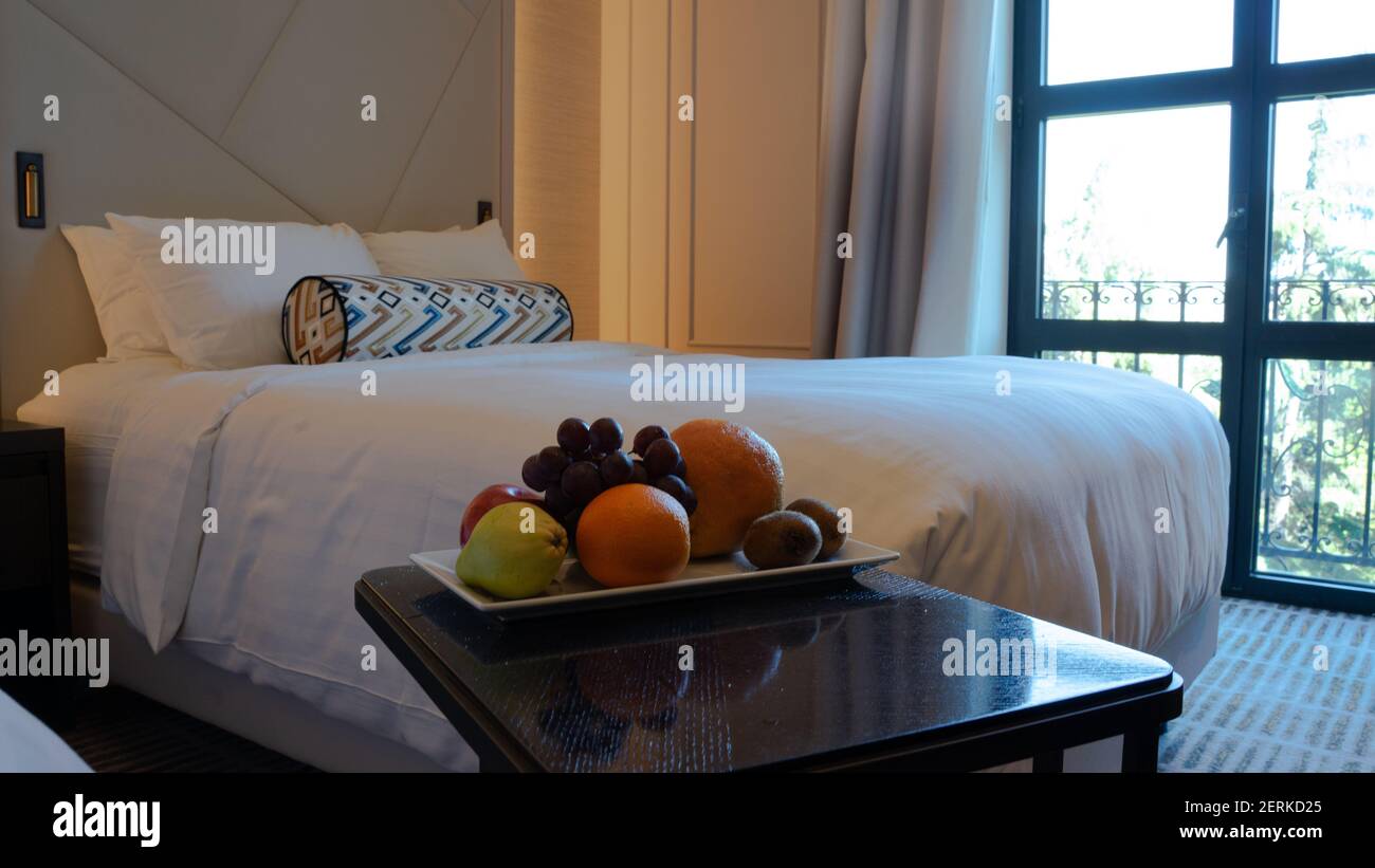 Ein Obstteller auf einem kleinen Tisch neben dem komfortablen, frisch zubereiteten Bett mit weißer Bettwäsche, Kissen und Bettwäsche Stockfoto