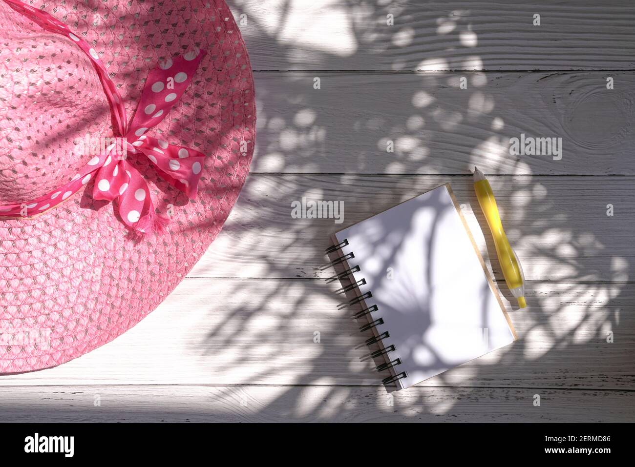 Notizblock und Stift mit rosa Sommerhut. Draufsicht mit Licht und Schatten. Stockfoto