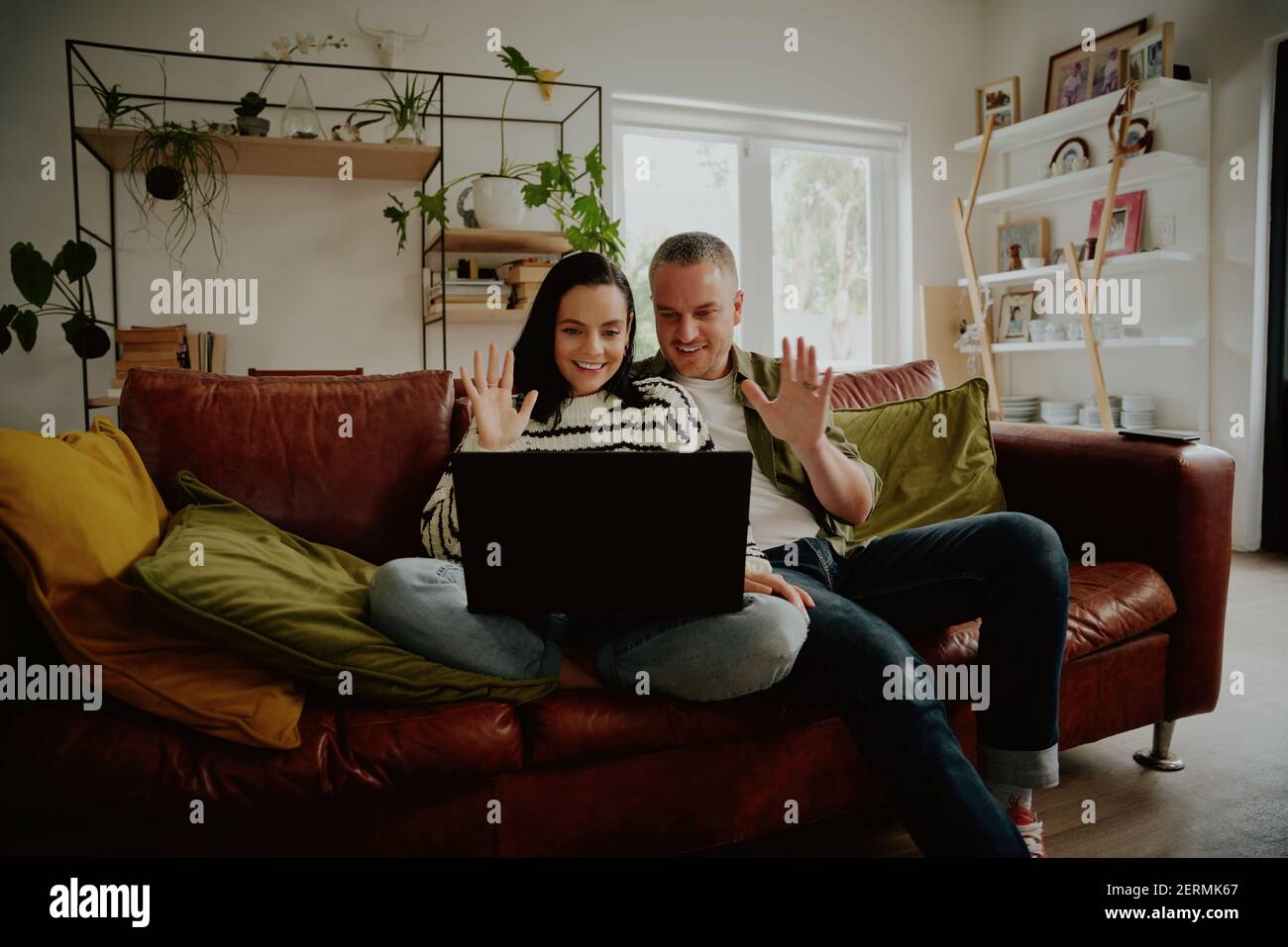 Fröhliches Paar sitzt auf dem Sofa und winkt die Hände zum Laptop Beim Chatten mit Videoanruf zu Hause Stockfoto