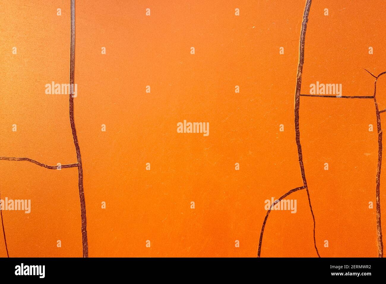 Rissige orangene Farbe an der Wand. Die Textur hat sich unter dem Einfluss atmosphärischer Einflüsse abgeschält. Hintergrund mit großen Rissen. Stockfoto