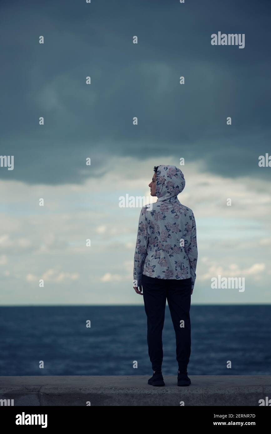 Rückansicht der Frau trägt floralen Kapuzenpullover auf dem stehen Blick auf den Strand Stockfoto