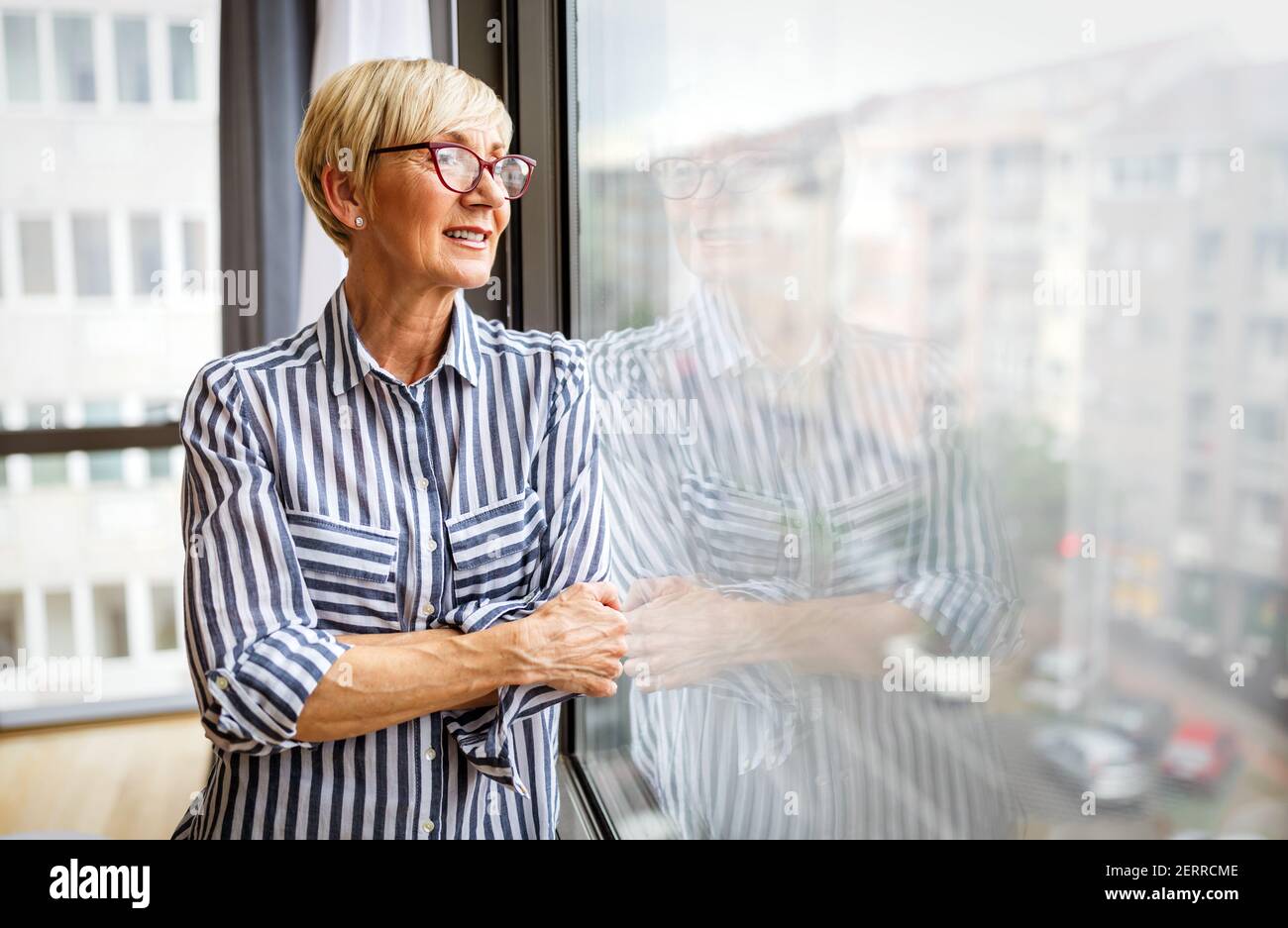 Ältere Frau, die am Fenster steht. Ruhestand, covid-19, Menschen Konzept Stockfoto