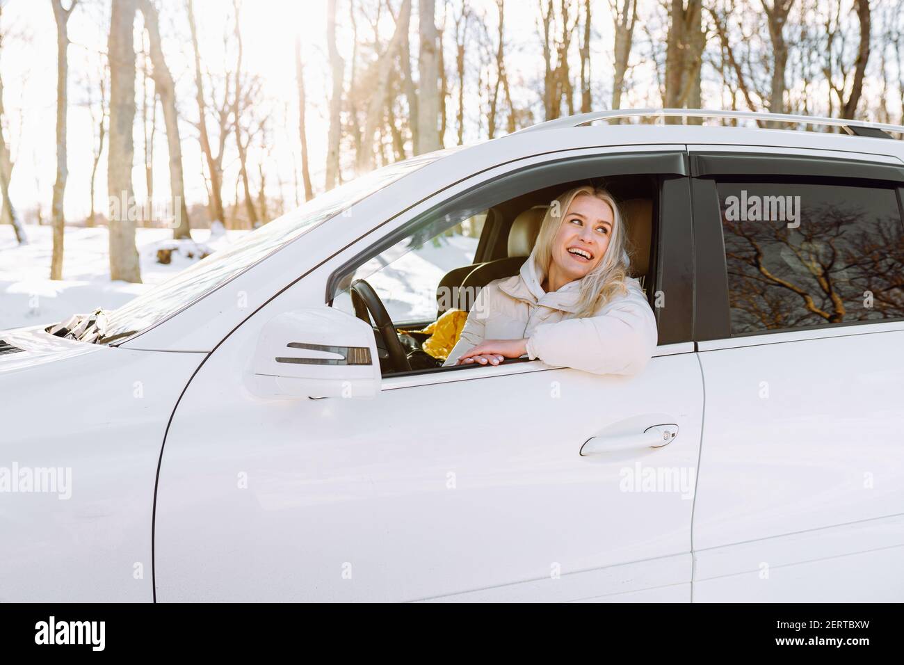 Junge blonde Frau sitzt in ihrem neuen weißen Auto und lächelt glücklich. Versicherung, Sicherheit. Stockfoto