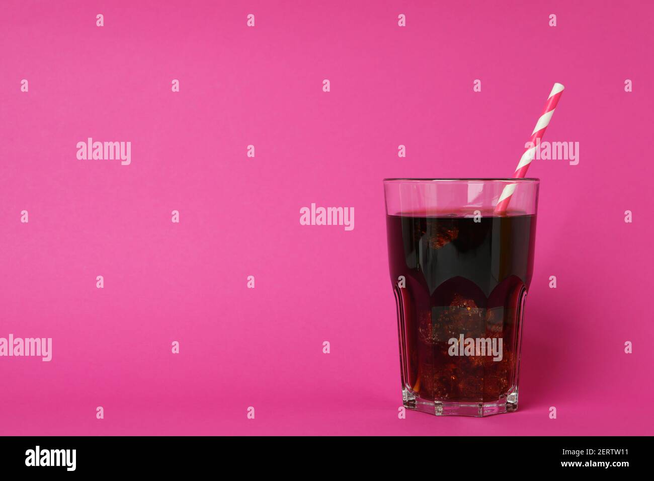 Glas Cola mit Eiswürfeln und Stroh auf rosa Hintergrund Stockfoto