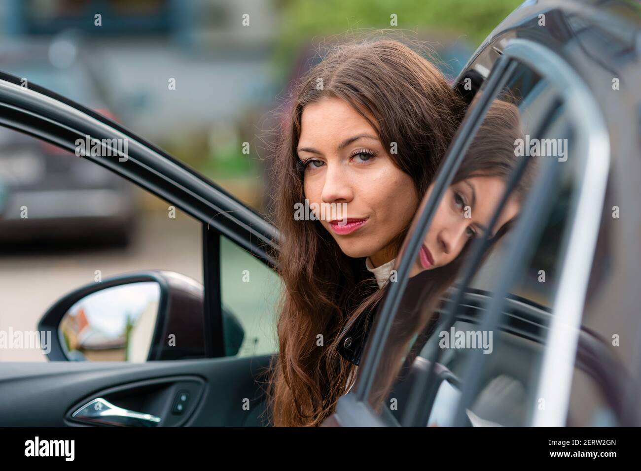 Die junge, lächelnde Frau sitzt in einem Auto mit offener Tür und blickt zurück, Nahaufnahme Porträt Stockfoto