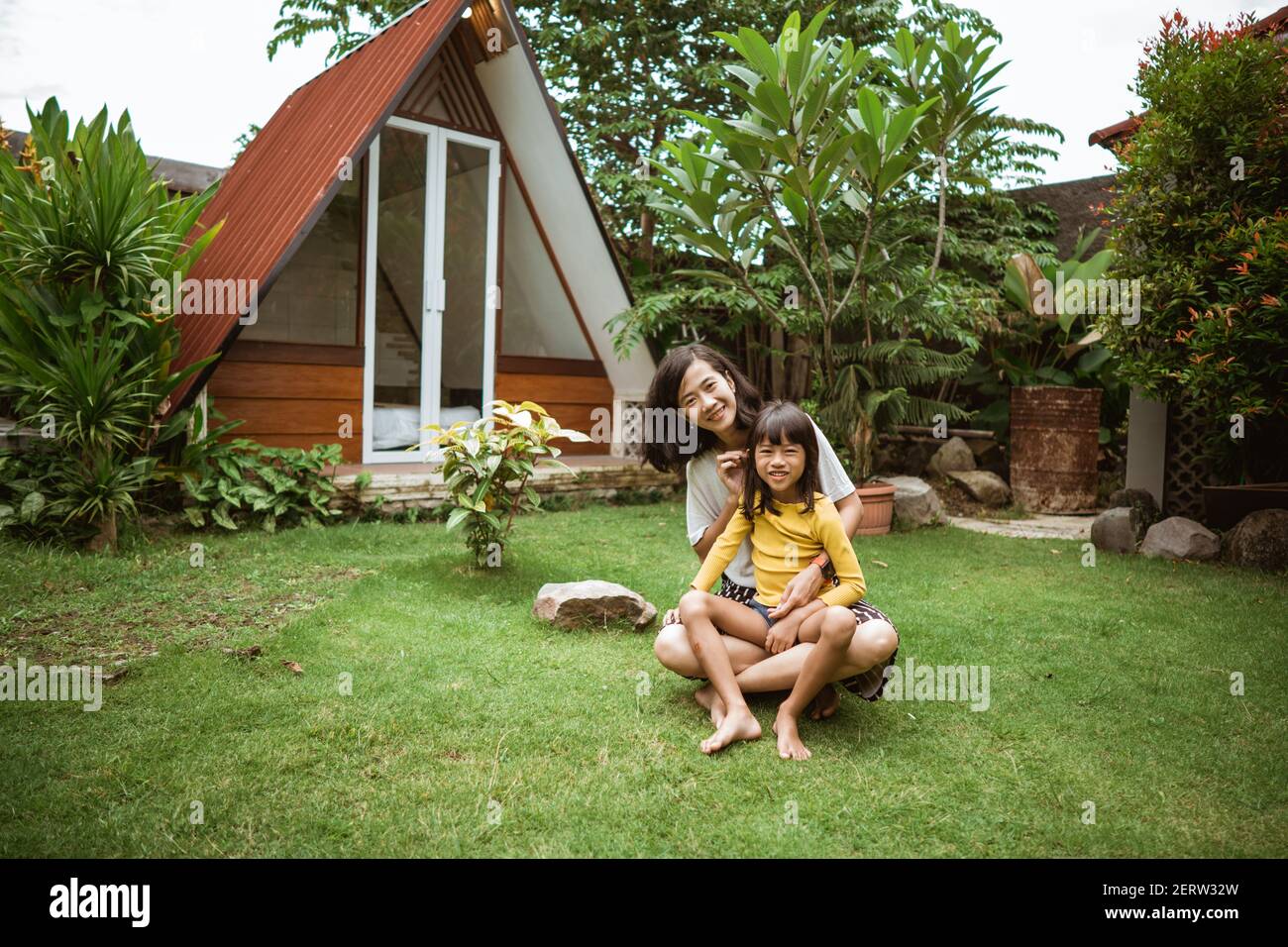 Nette kleine asiatische Mädchen Unterstützung ihrer Mutter spielen und haben Spaß in einem Hinterhof. Stockfoto