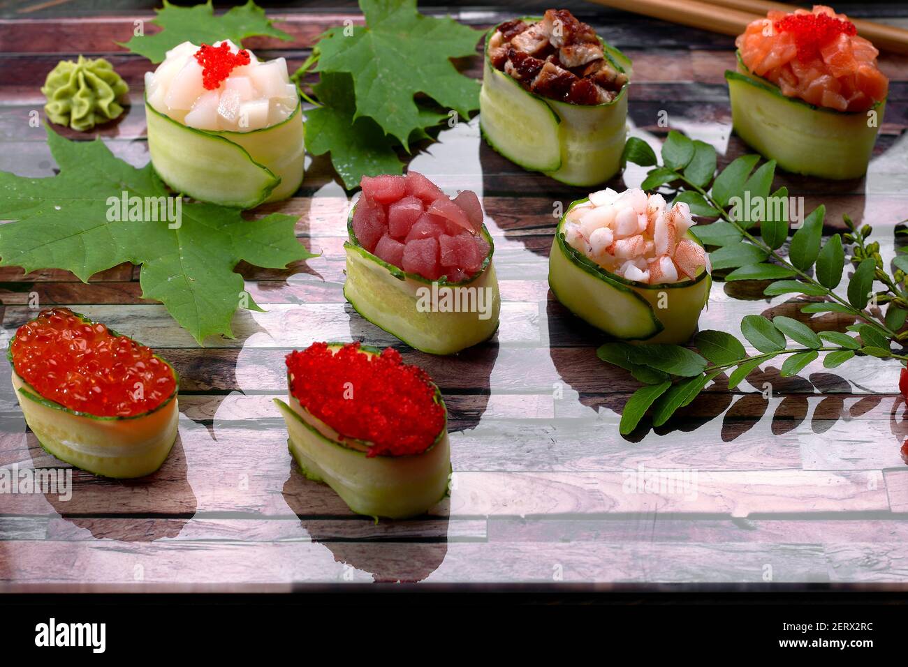 Gunkan Maki in einer Gurke, mit Kaviar, Thunfisch. Jakobsmuschel, Aal, Garnelen, Aal und Lachs, Auf einem Holzbrett, mit Ahorn und Akazienblättern, mit geringer Tiefe Stockfoto