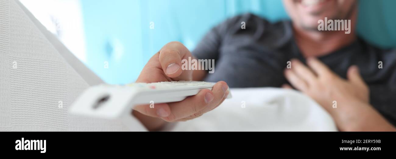 Der Mensch liegt auf dem Bett und hält die Fernbedienung in den Händen. Stockfoto