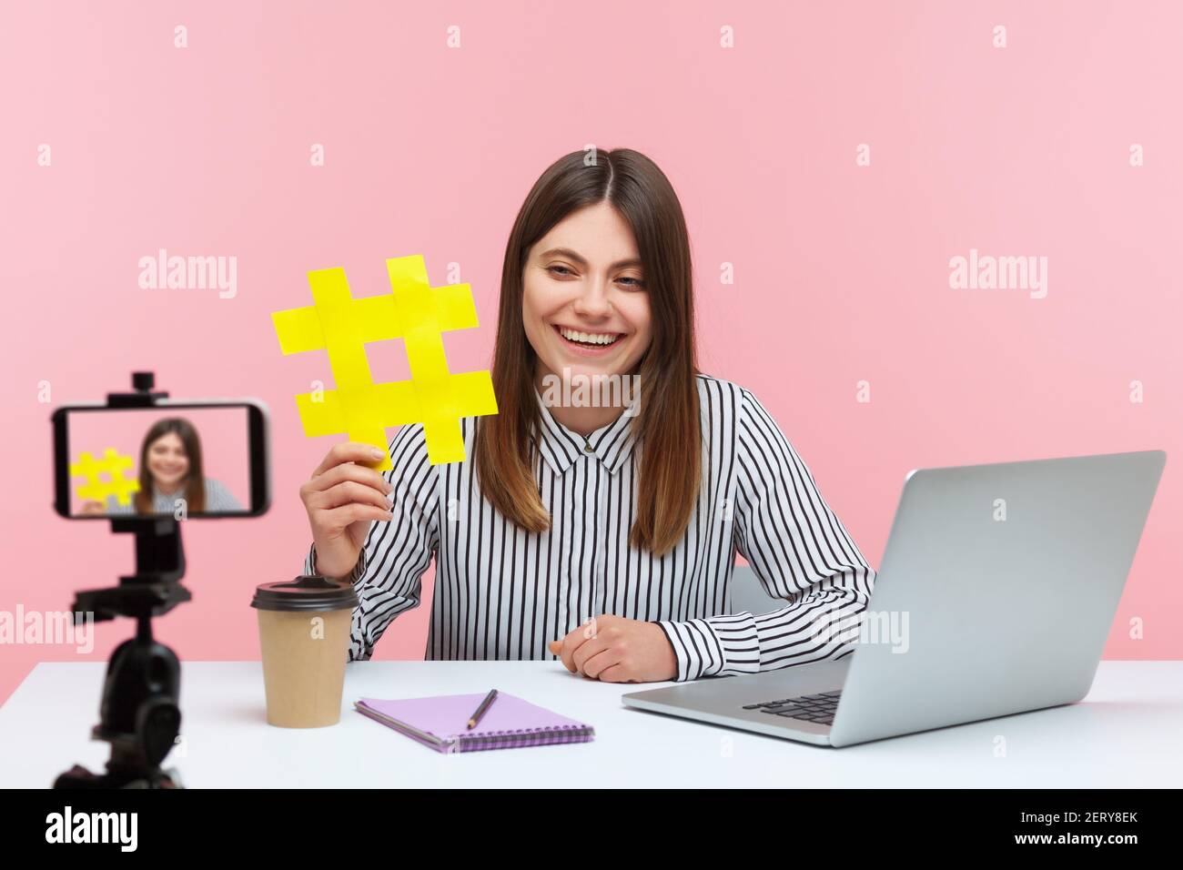 Lächelnd attraktive Frau blogger zeigt große gelbe Hashtag-Symbol auf Smartphone-Kamera, teilen viralen Inhalt, getaggte Nachricht. Innenaufnahmen im Studio iso Stockfoto