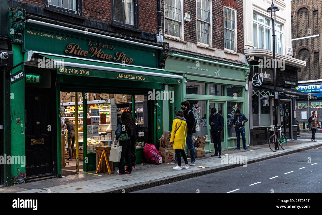 Eine kurze Schlange von Kunden vor einem japanischen Lebensmittelgeschäft, Brewer Street, Soho, London, England, VEREINIGTES KÖNIGREICH. Stockfoto