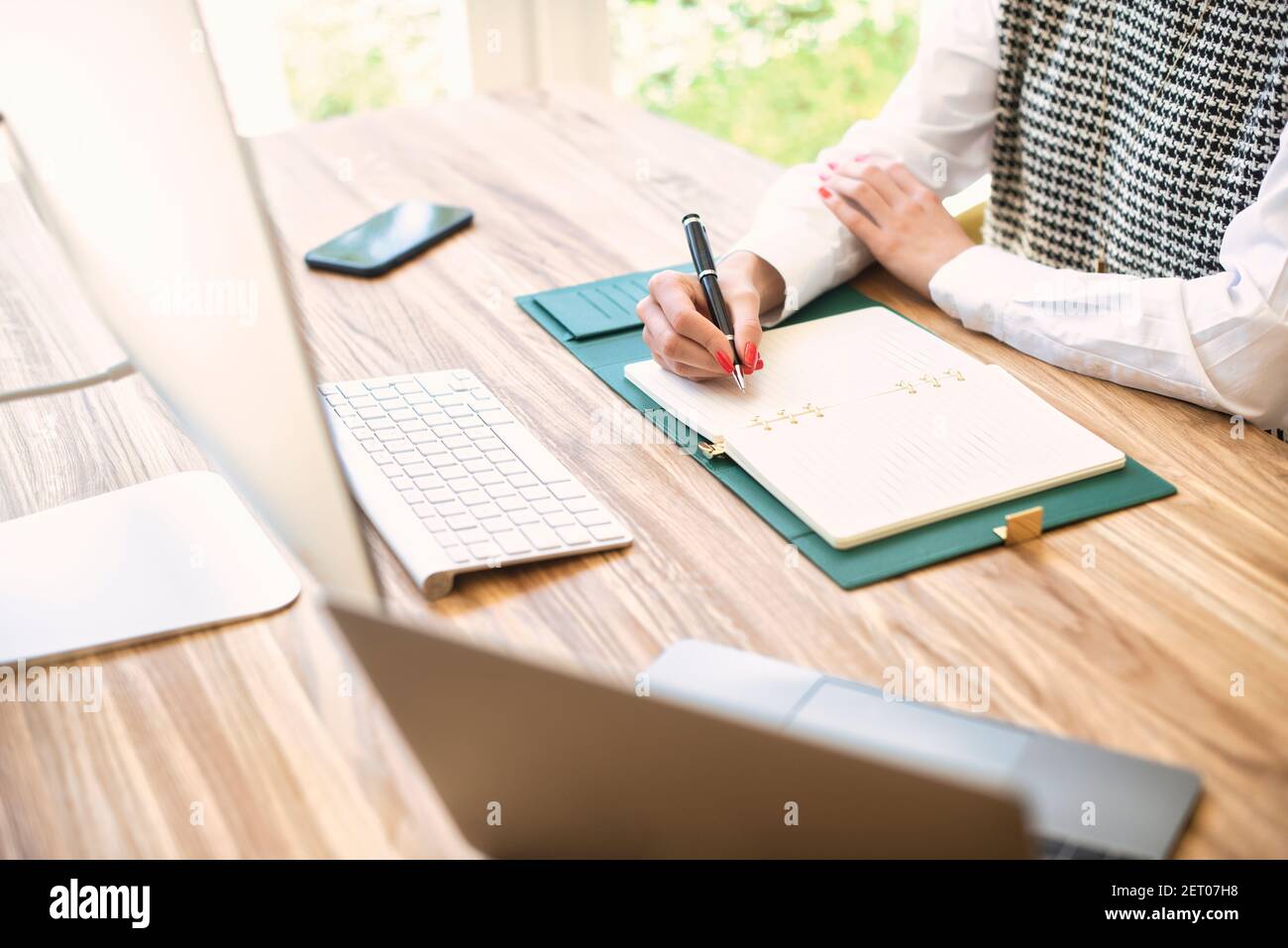 High-Angle-Aufnahme einer nicht erkennbaren Geschäftsfrau, die am Schreibtisch sitzt und etwas in ihr Notebook schreibt. Stockfoto