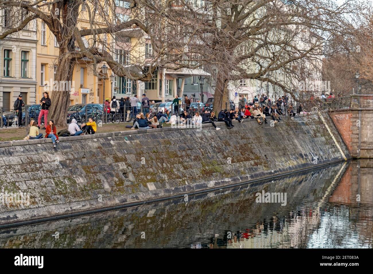Junge Leute sitzen am Landwehrkanal in Kreuzberg, Urbanhafen, Berlin, Vorfruehling, Lockdown, Aha-Regeln, Stockfoto