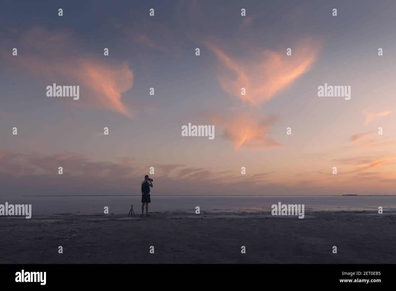 Fotograf, der mit einem Stativ des Ozeanaufgangs fotografiert. Sonnenuntergang auf dem Meer mit rot glühenden wolkigen Himmel. Landschaftsfotografie Stockfoto