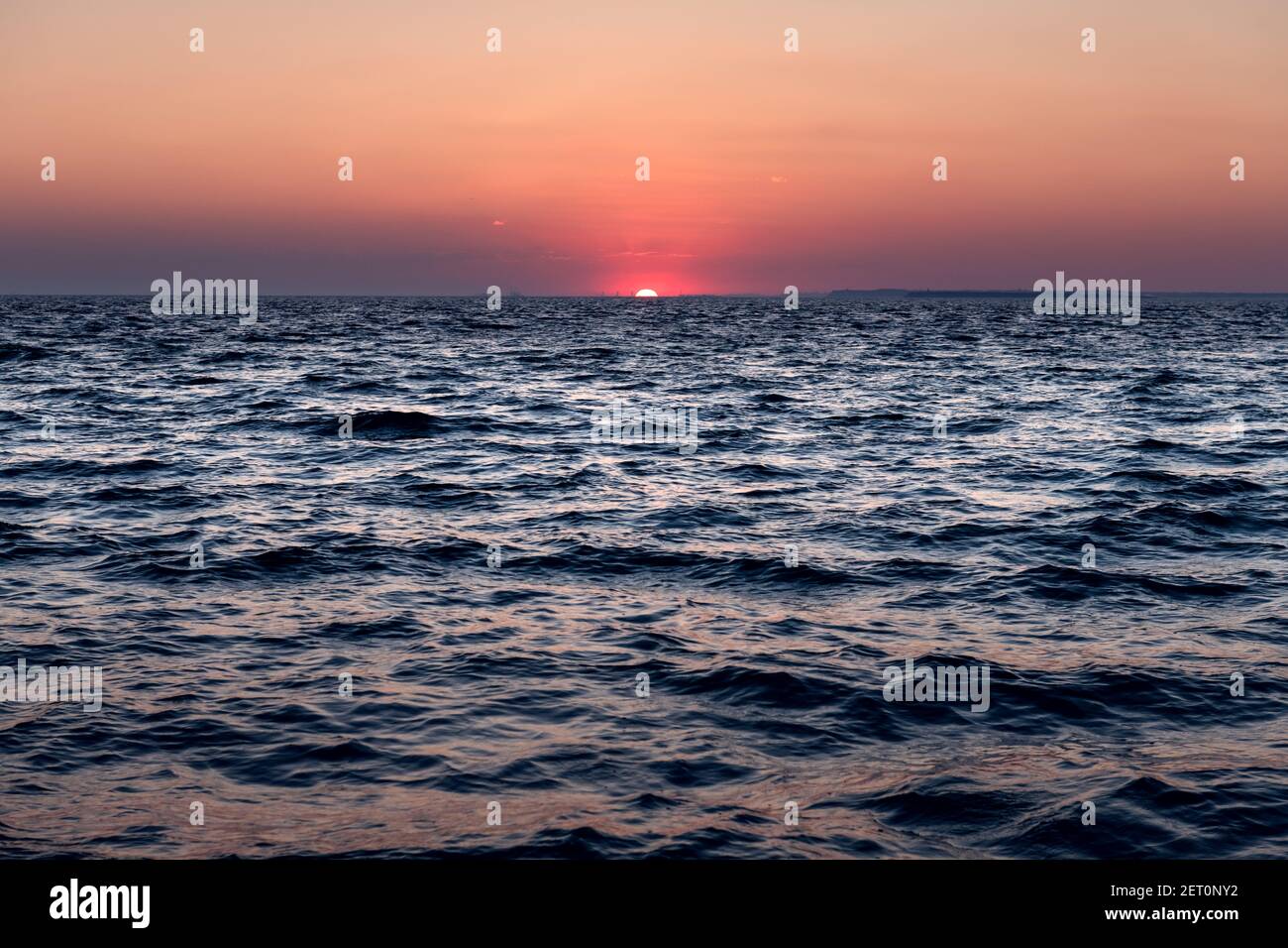 Sonnenuntergang im Meer mit großer Sonnendämmerung sanfte Wellen und rot bewölkter Himmel. Hintergrund des Sonnenaufgangs. Landschaftsfotografie Stockfoto