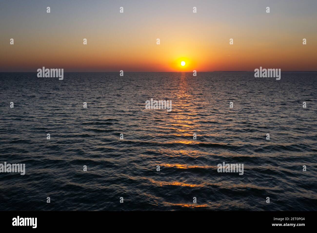 Sonnenuntergang im Meer mit großer Sonnendämmerung sanfte Wellen und rot bewölkter Himmel. Hintergrund des Sonnenaufgangs. Landschaftsfotografie Stockfoto