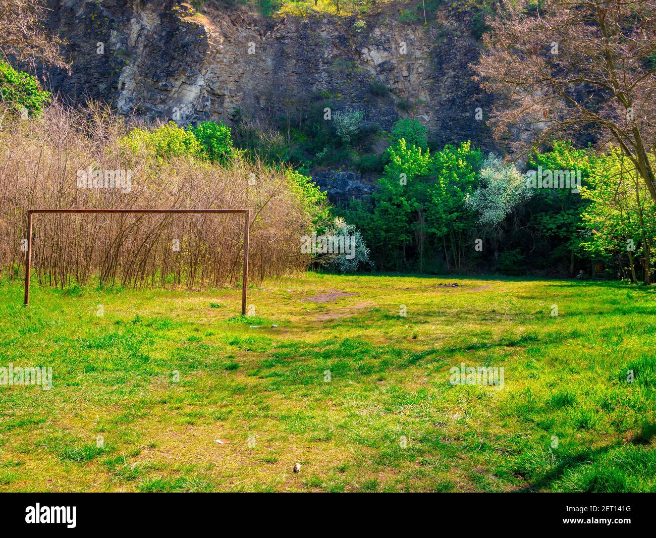 Ein verlassene Fußballplatz mit einem rostenden Fußballtor langsam von Grün überwuchert, unter einem Felsen Stockfoto