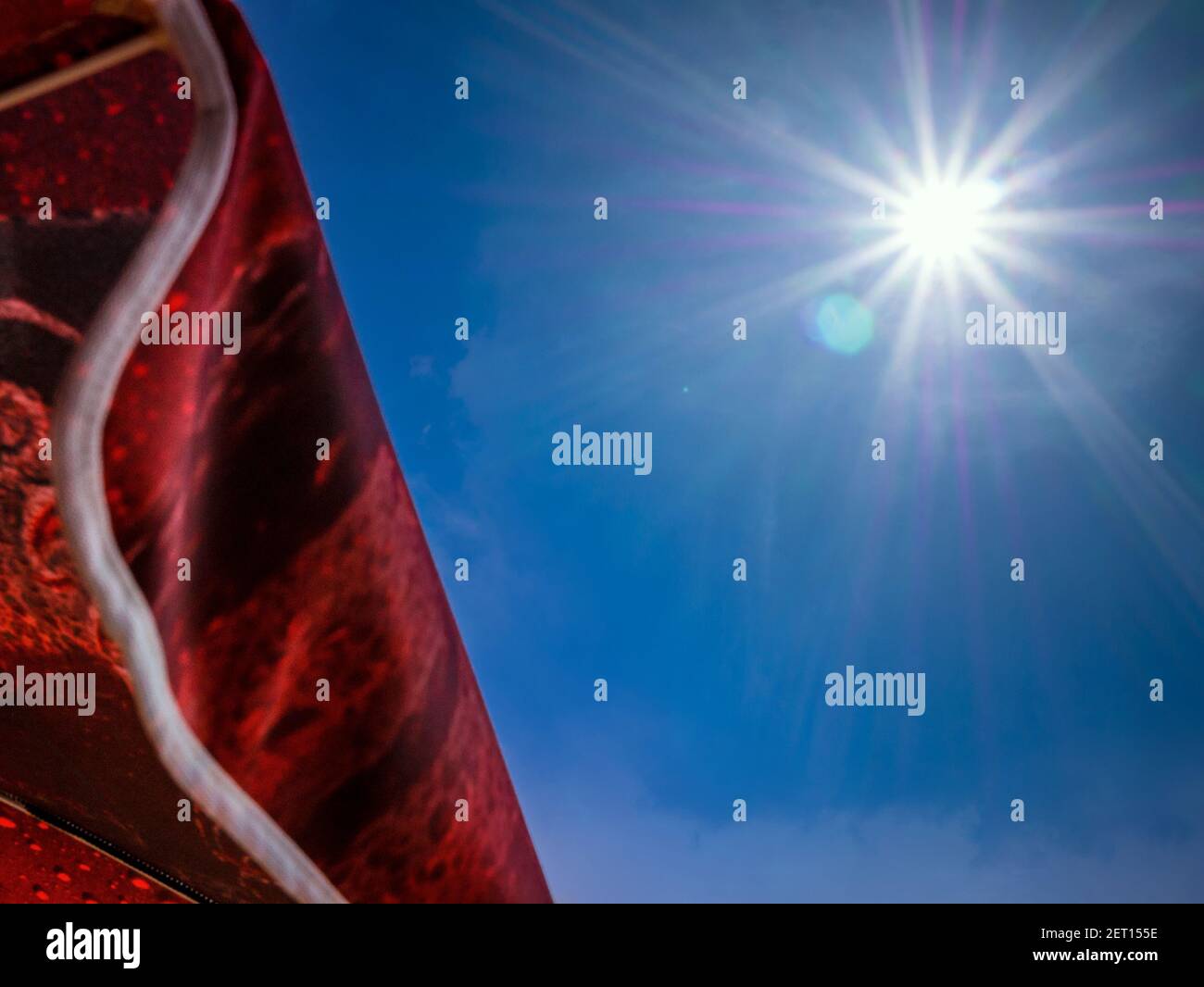 Ein roter Sonnenschirm gegen fast klaren blauen Himmel mit Sonne Und Sonneneinstrahlung Stockfoto