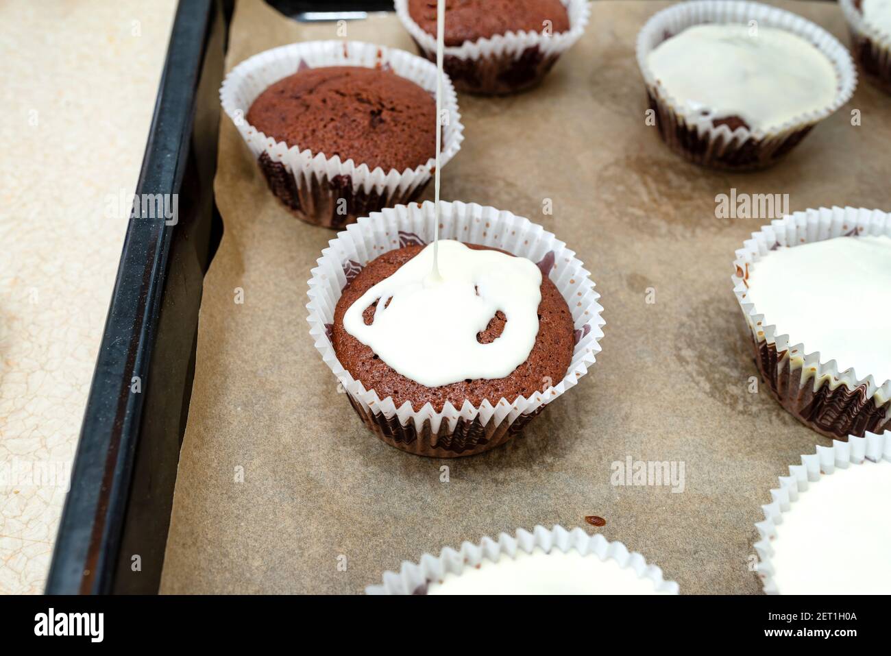 Schokoladen-Muffin-Kuchen braun in weißem Papier gewickelt und mit weißem  Zuckerguss bedeckt, im Ofen gebacken, auf Backpapier liegend  Stockfotografie - Alamy