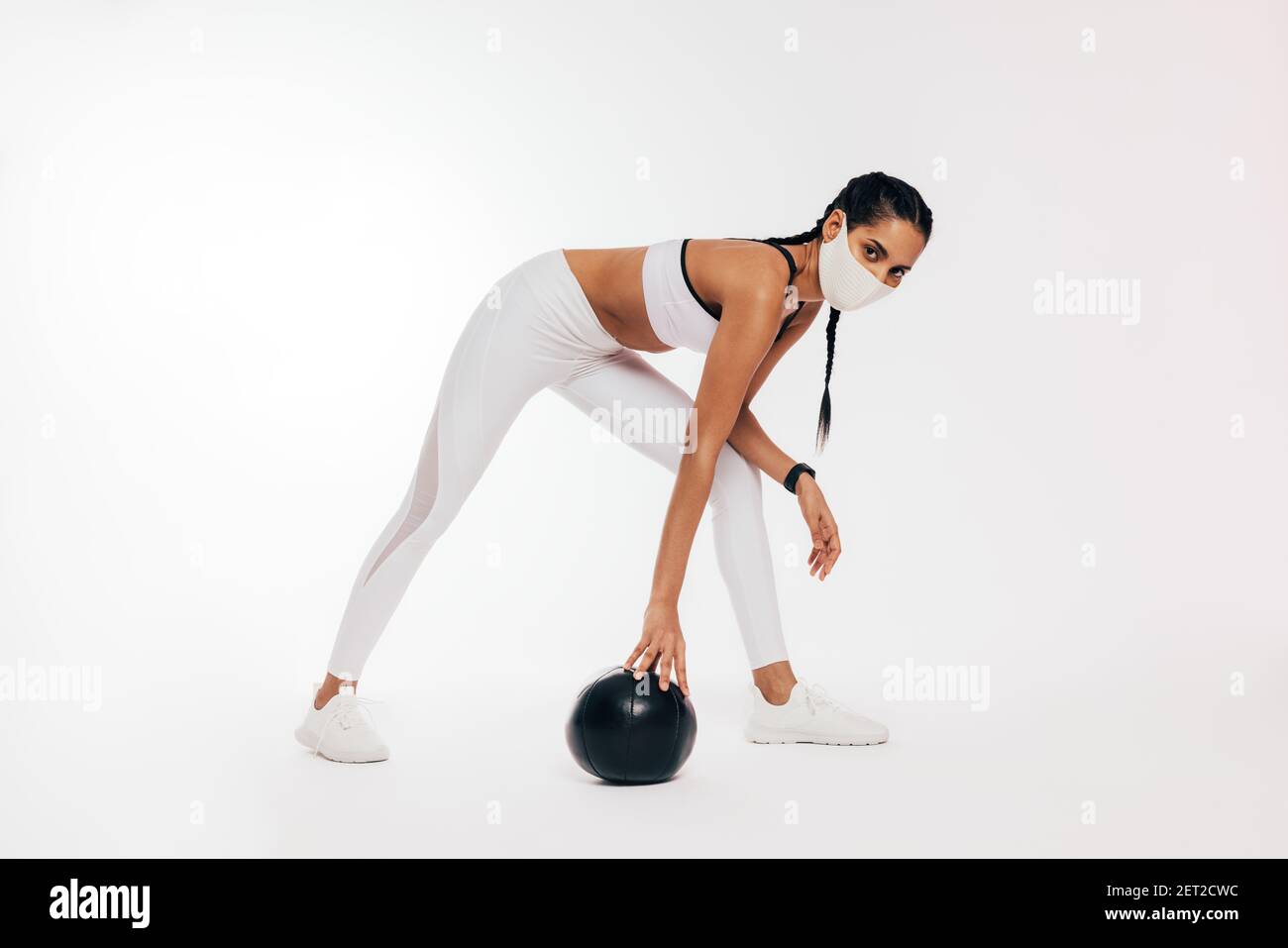 Junge Frau in Sportbekleidung mit Schutzmaske trainieren mit Medizinball Stockfoto
