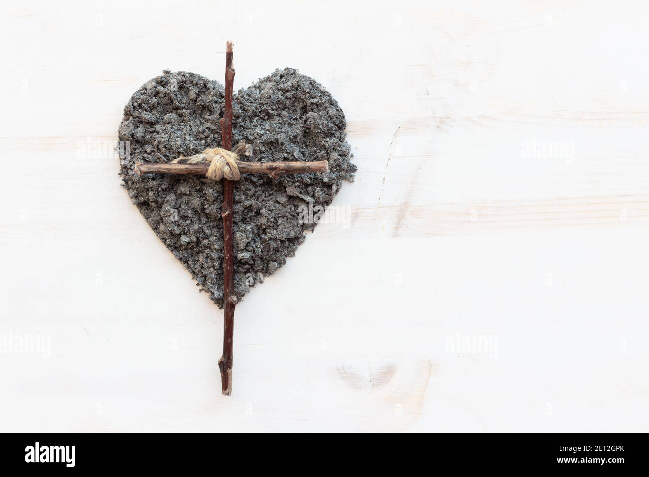 Einfaches christliches Holzkreuz und ein Herz aus Asche auf weißem Holzhintergrund mit Kopierraum Stockfoto