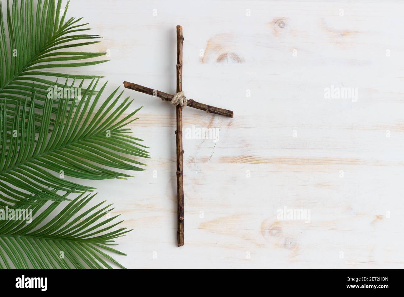 Holzkreuz mit Palmwedeln auf weißem Holzhintergrund Stockfoto