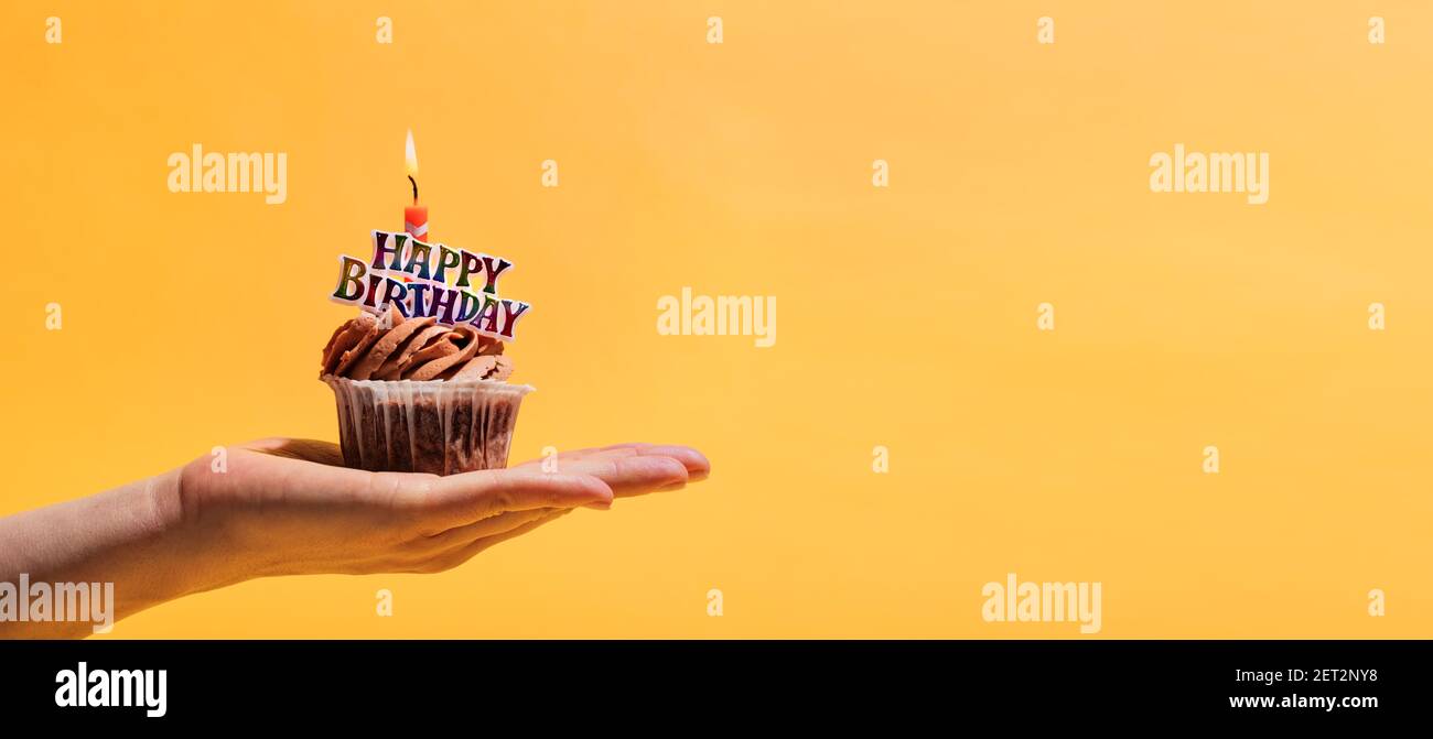 Frau Hand halten geschmückt Geburtstag Muffin vor gelbem Hintergrund. Geburtstagsfeier und Feier. Stockfoto