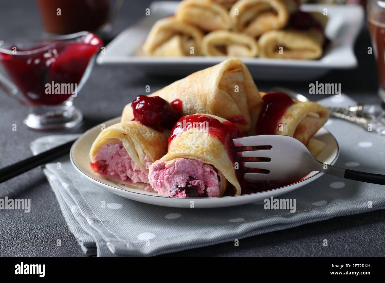 Hausgemachte Pfannkuchen mit Quark Füllung und Kirsche, serviert mit Kirschsauce auf einem Teller auf dunklem Hintergrund. Stockfoto