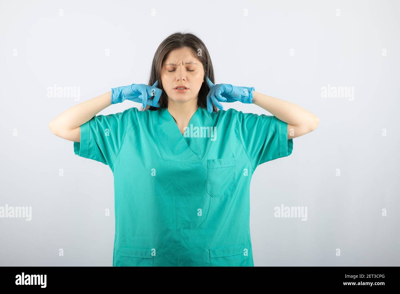 Junge Ärztin in grüner Uniform, die Ohren mit Index bedeckt Finger Stockfoto