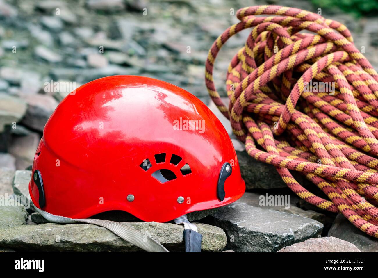 Seilzugangswerkzeuge: Schutzhelm, Seil, Karabiner. Bergsport Ausrüstung auf Felsen vor einem Hintergrund von Felsen und Grün Stockfoto