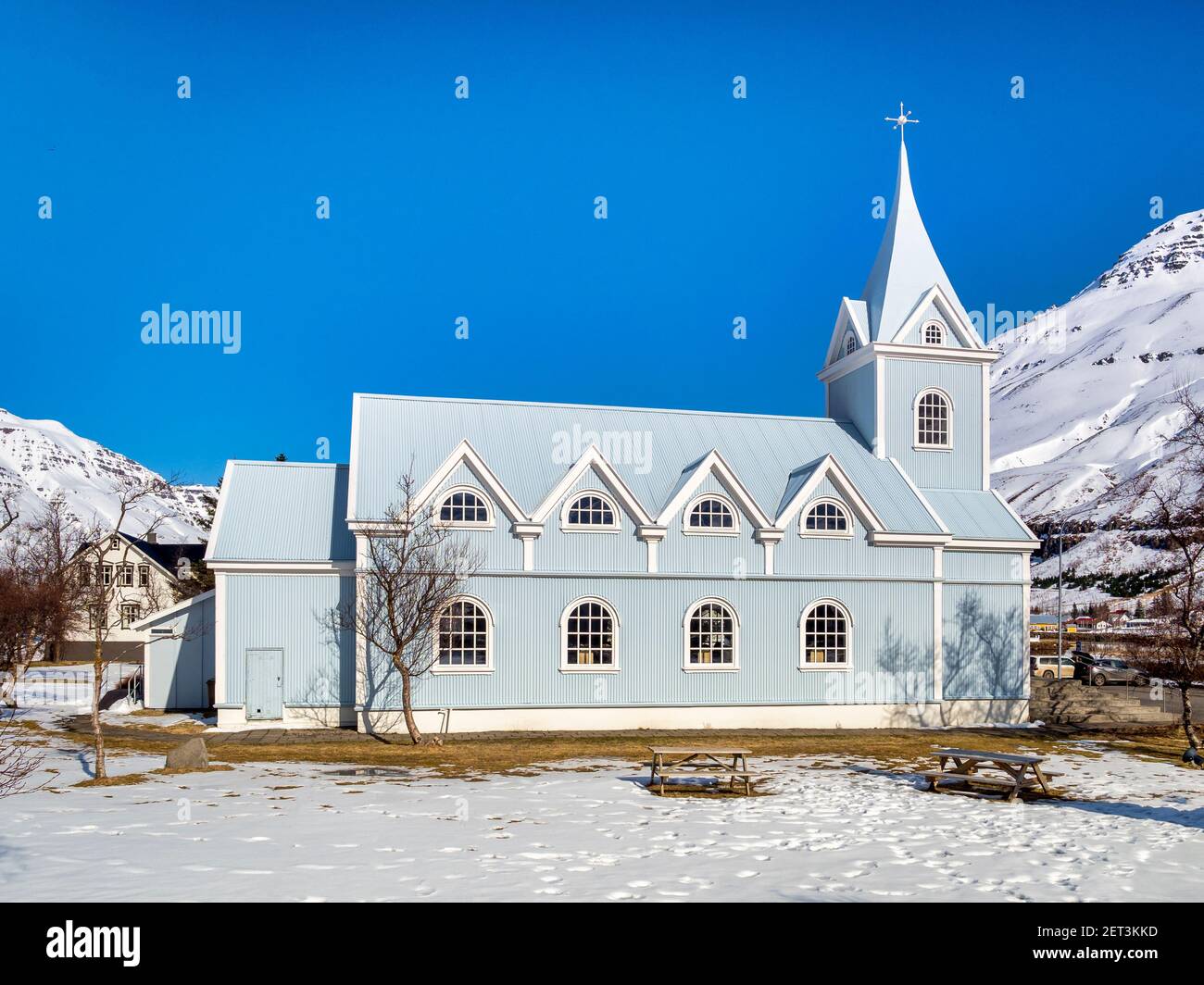 Die berühmte Blaue Kirche in Seydisfjördur, Osten Island, an einem strahlenden Frühlingstag mit schneebedeckten Bergen. Stockfoto