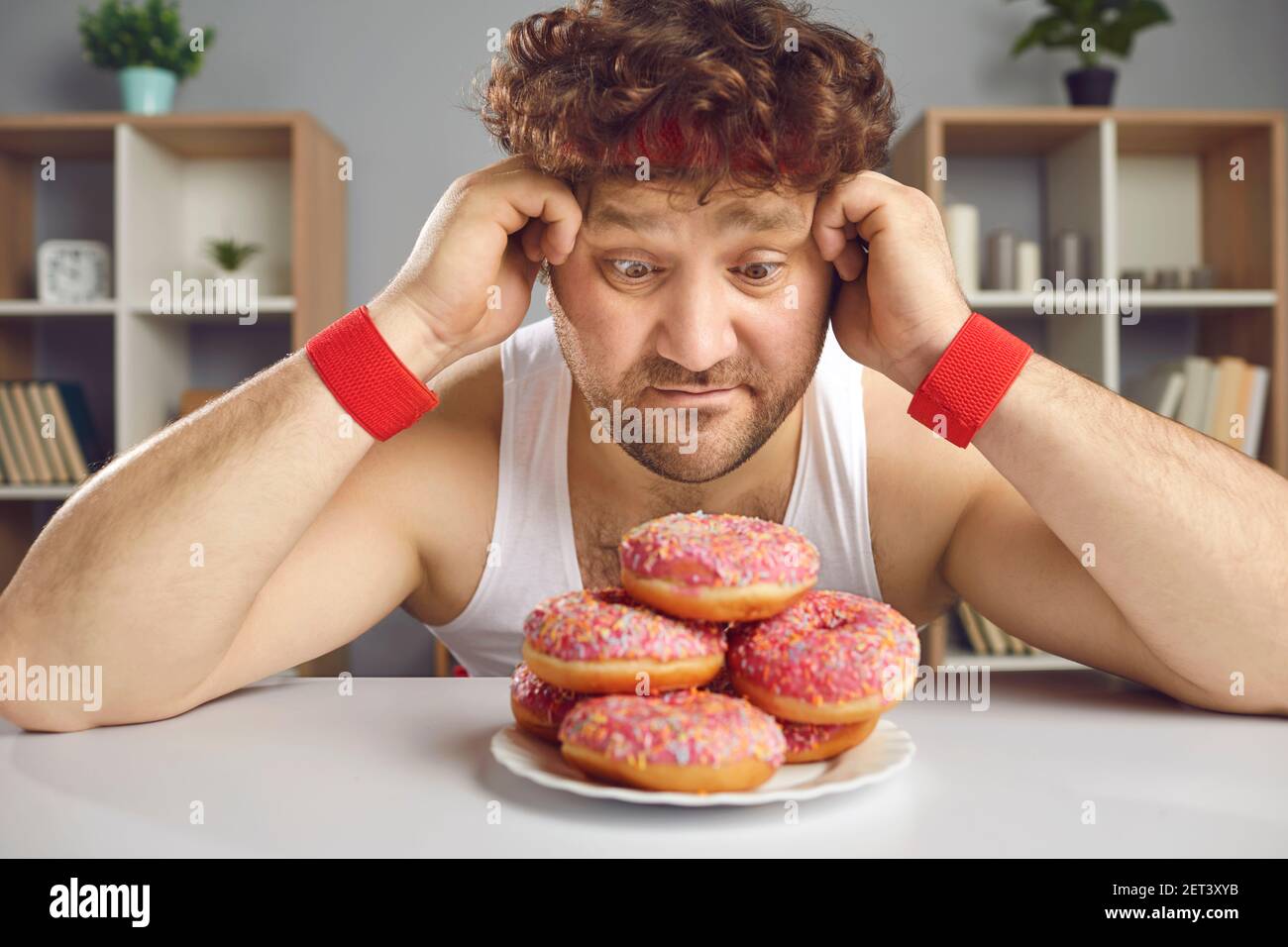 Lustige Mann, der ungesunde süße Lebensmittel liebt wird versucht Von leckeren Donuts Stockfoto