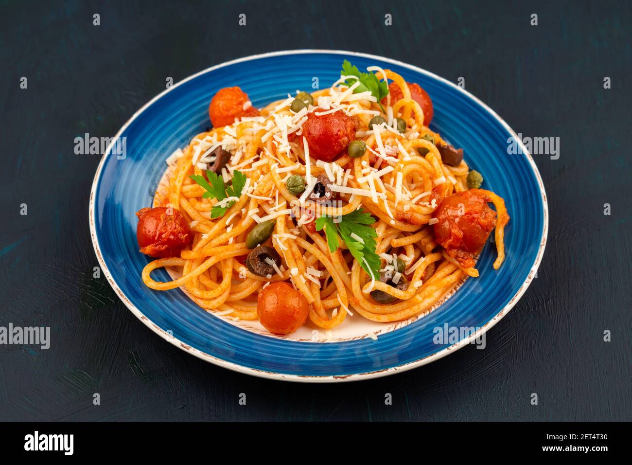 Pasta Spaghetti Puttanesca auf blauem Teller auf dunklem Holzhintergrund. Italienische Küche. Stockfoto