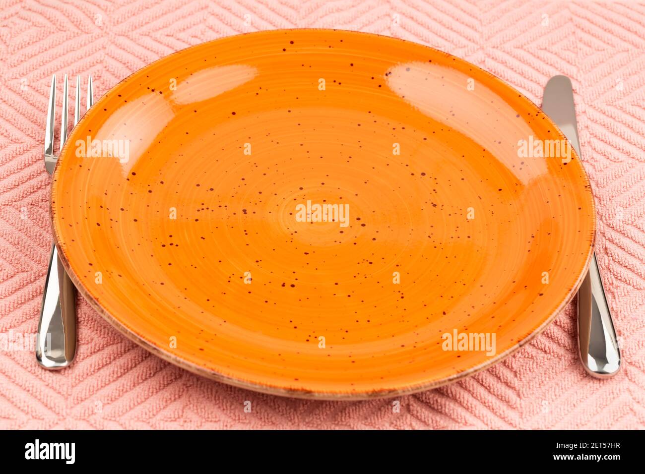 Orange leerer Teller mit Messer und Gabel auf rosa Baumwolltuch. Stockfoto