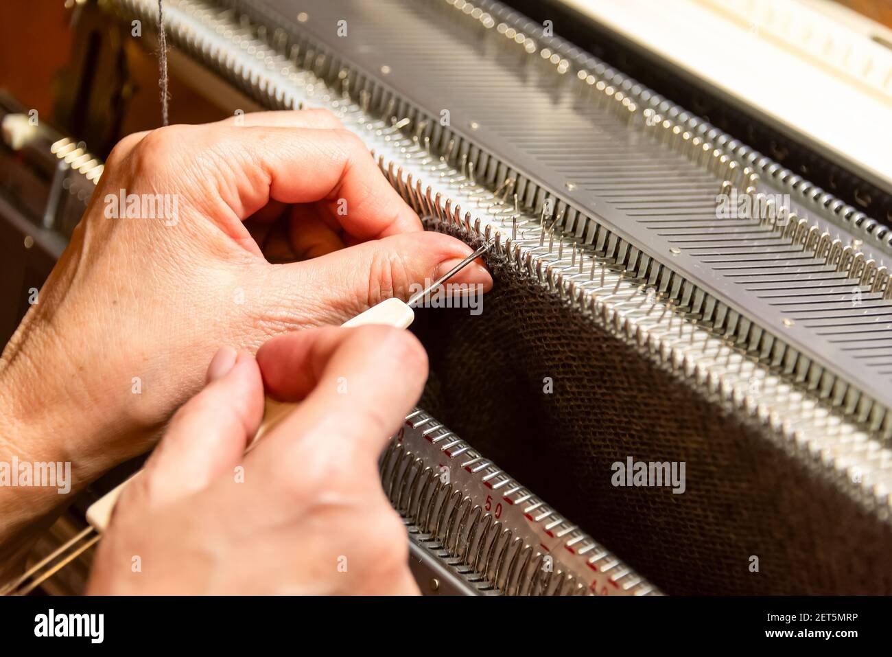 Womans Hände arbeiten mit Strickmaschine, Stricken als Womans Hobbys. Kleines Geschäft der Bekleidungsherstellung, langsame Mode Stockfoto