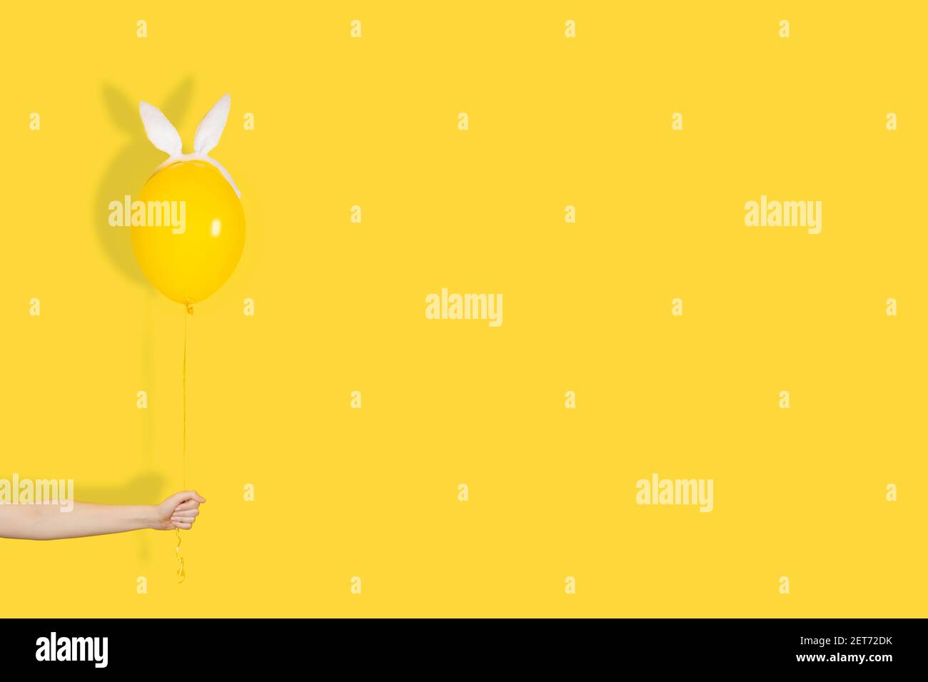 Kreatives osterkonzept. Hand hält einen gelben Ballon in Hasenohren. Monochrom. Banner mit Kopierbereich Stockfoto