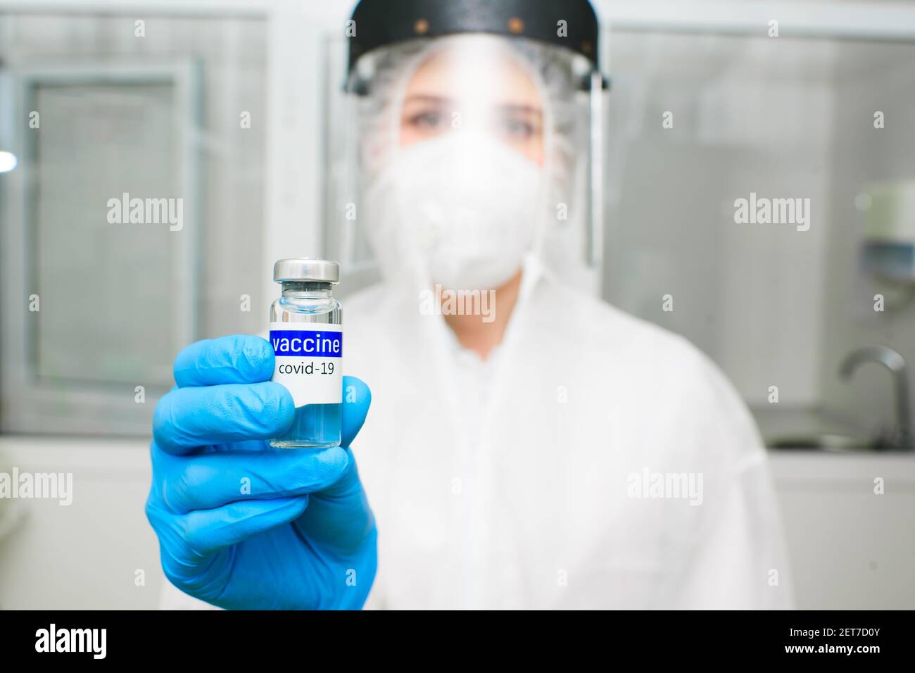 Arzt oder PCR-Laborforscher in Schutzkleidung, Helm und Atemschutzmaske hält eine Flasche mit der Aufschrift covid-19 Impfstoff Stockfoto