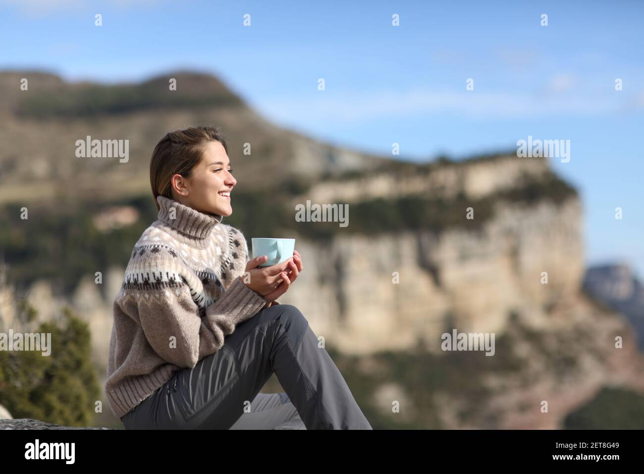 Glücklicher Wanderer, der Kaffee trinkt und dabei die Aussicht betrachtet, in der er sitzt Der Berg im Winter Stockfoto