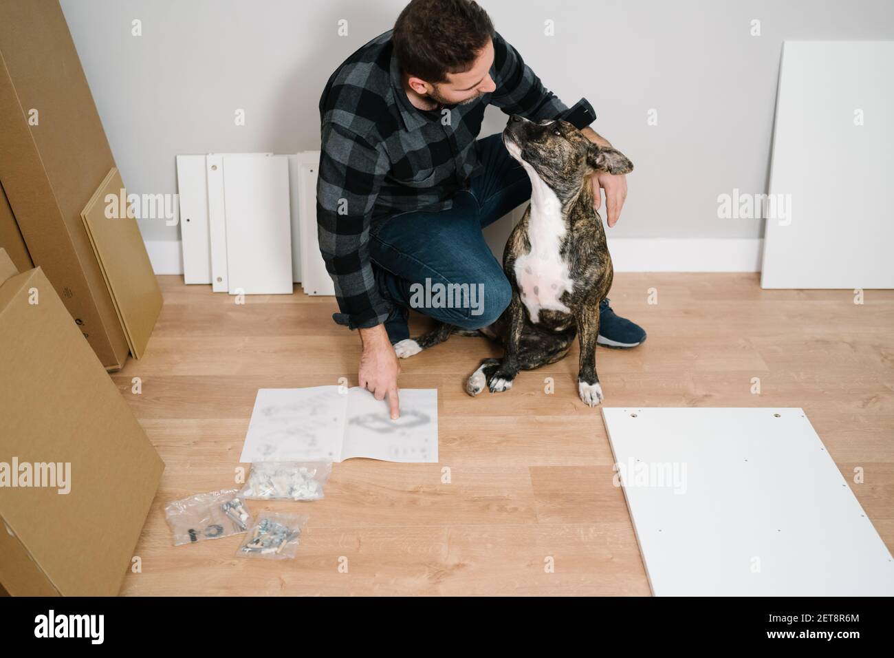 Mann spielt mit seinem Hund, während er selbst ein Möbelstück zusammenstellt. Machen Sie es selbst Stockfoto
