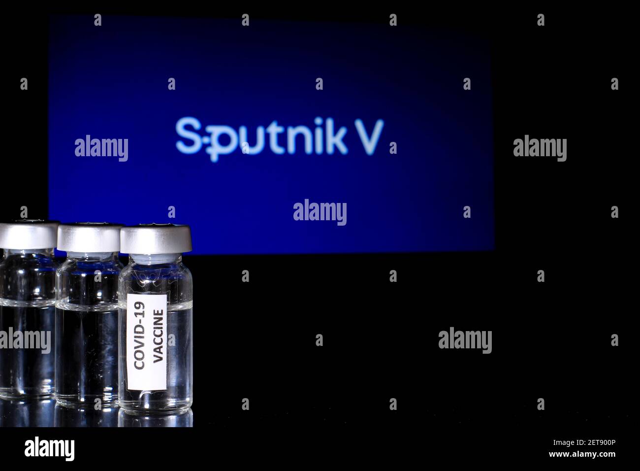 Madrid, Spanien - 23. Februar 2021: Glasfläschchen mit Covid-19-Impfstoff auf schwarzem Hintergrund. Sputnik V Logo im Hintergrund. Stockfoto