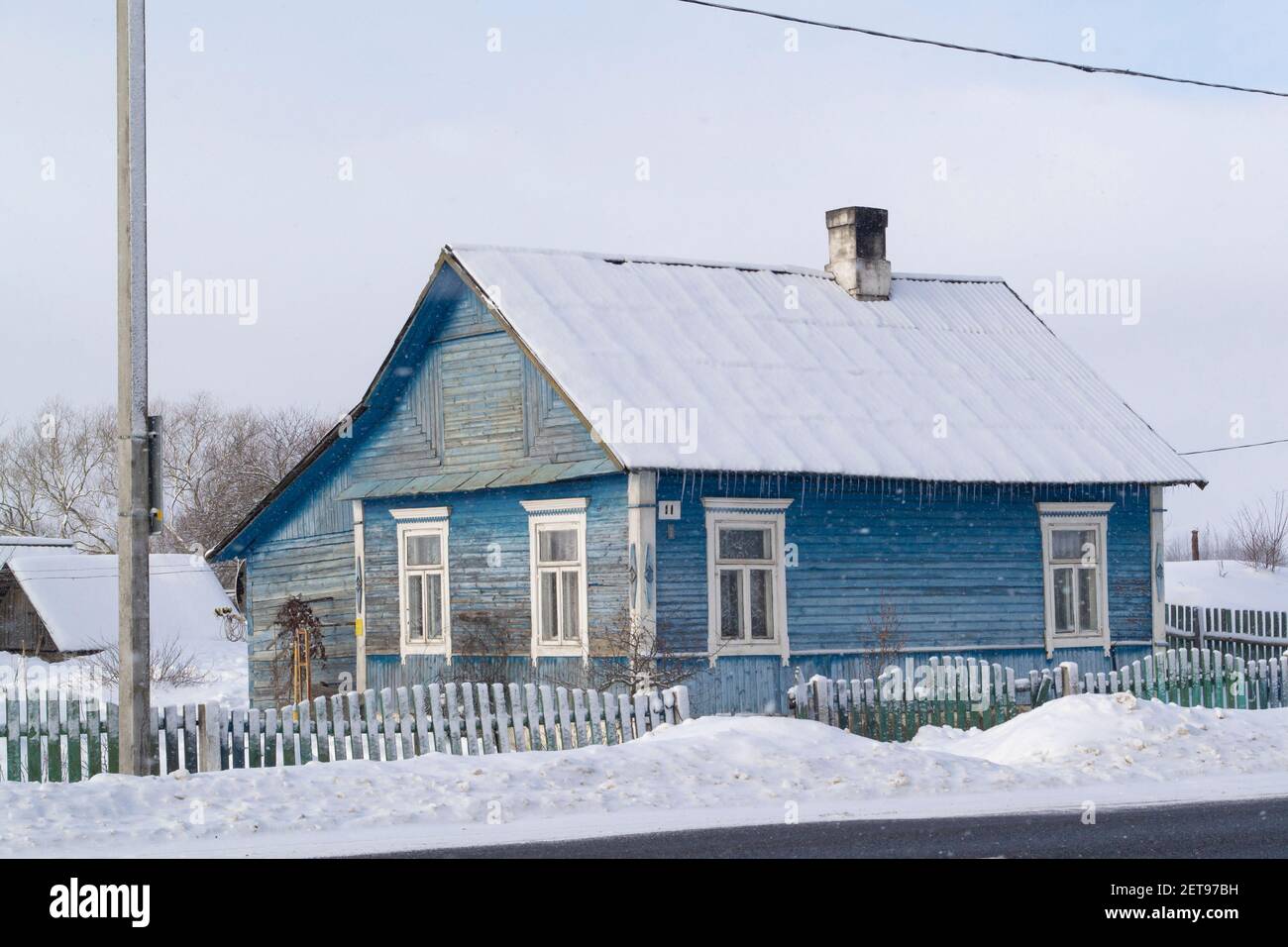 Altes blaues Holzhaus im Dorf. Bauernhaus in Weißrussland. Blick auf rustikales Volkshaus, ländliche Landschaft im Winter Stockfoto