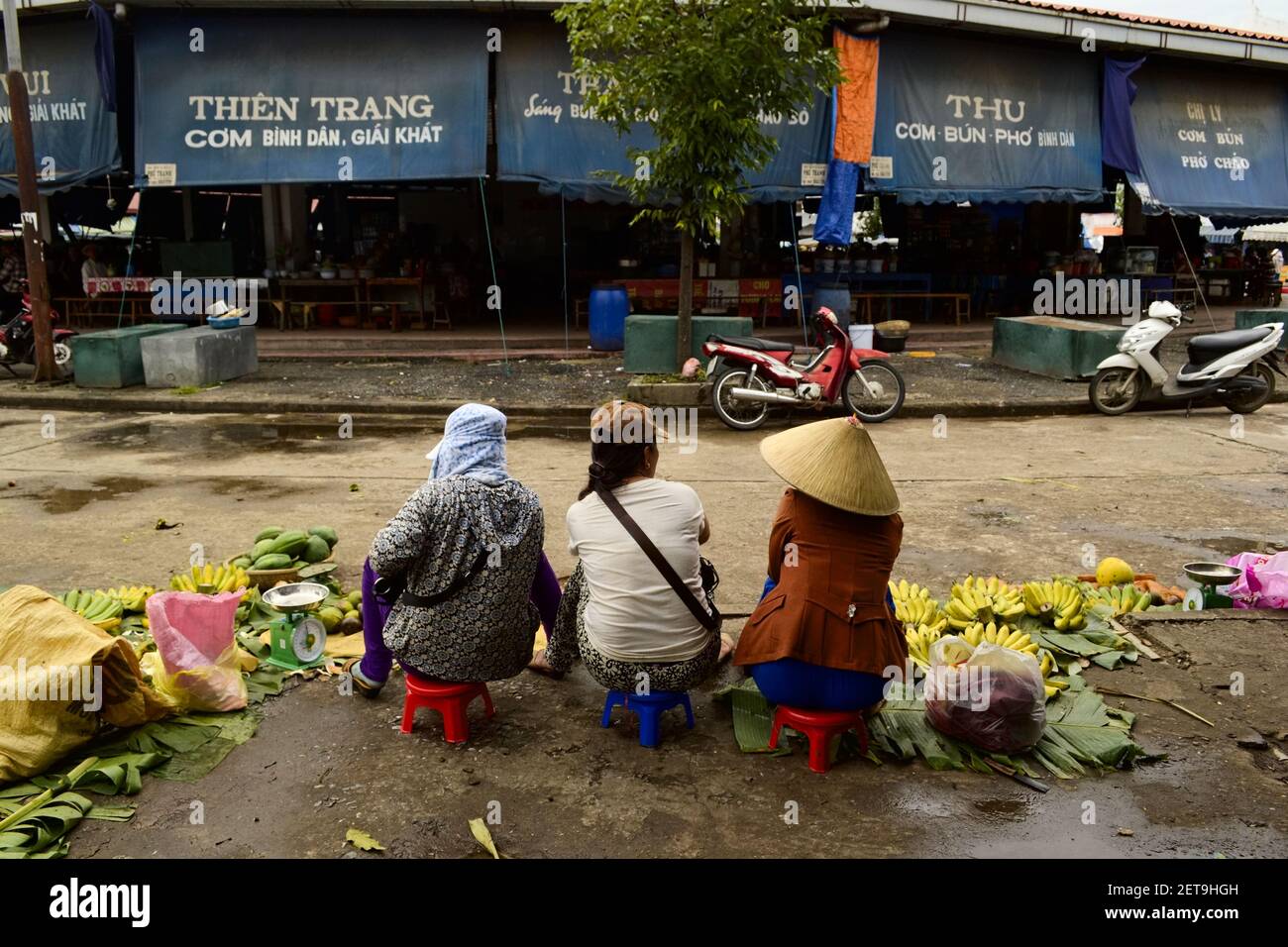 Dong Ha, Vietnam - September, 2015: Drei Frauen sitzen auf kleinen Stühlen und verkaufen Bananen und Gemüse auf einem traditionellen Straße asiatischen Markt. Stockfoto