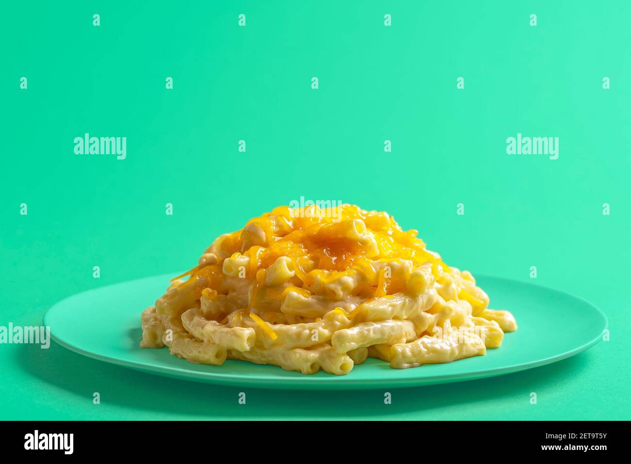 Teller mit mac und Käse isoliert auf grünem Hintergrund. Makkaroni mit Bechamelsauce und geschmolzenem Cheddar-Käse auf einem grünen Teller. Stockfoto