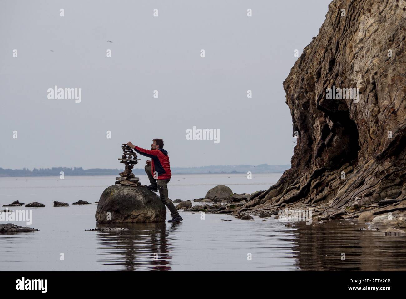 FUR, DÄNEMARK - 21. Feb 2021: Steinbalance-Künstler arbeitet an einem Kunstwerk im Wasser auf der dänischen Insel fur. Steht im Wasser unter einer fossilen Klippe Stockfoto