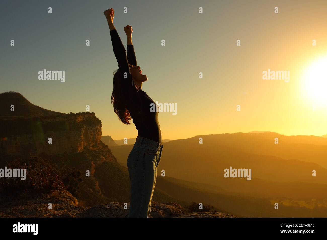 Profil einer Silhouette einer Frau, die die Arme hebt Wir feiern Urlaub bei Sonnenuntergang in den Bergen Stockfoto
