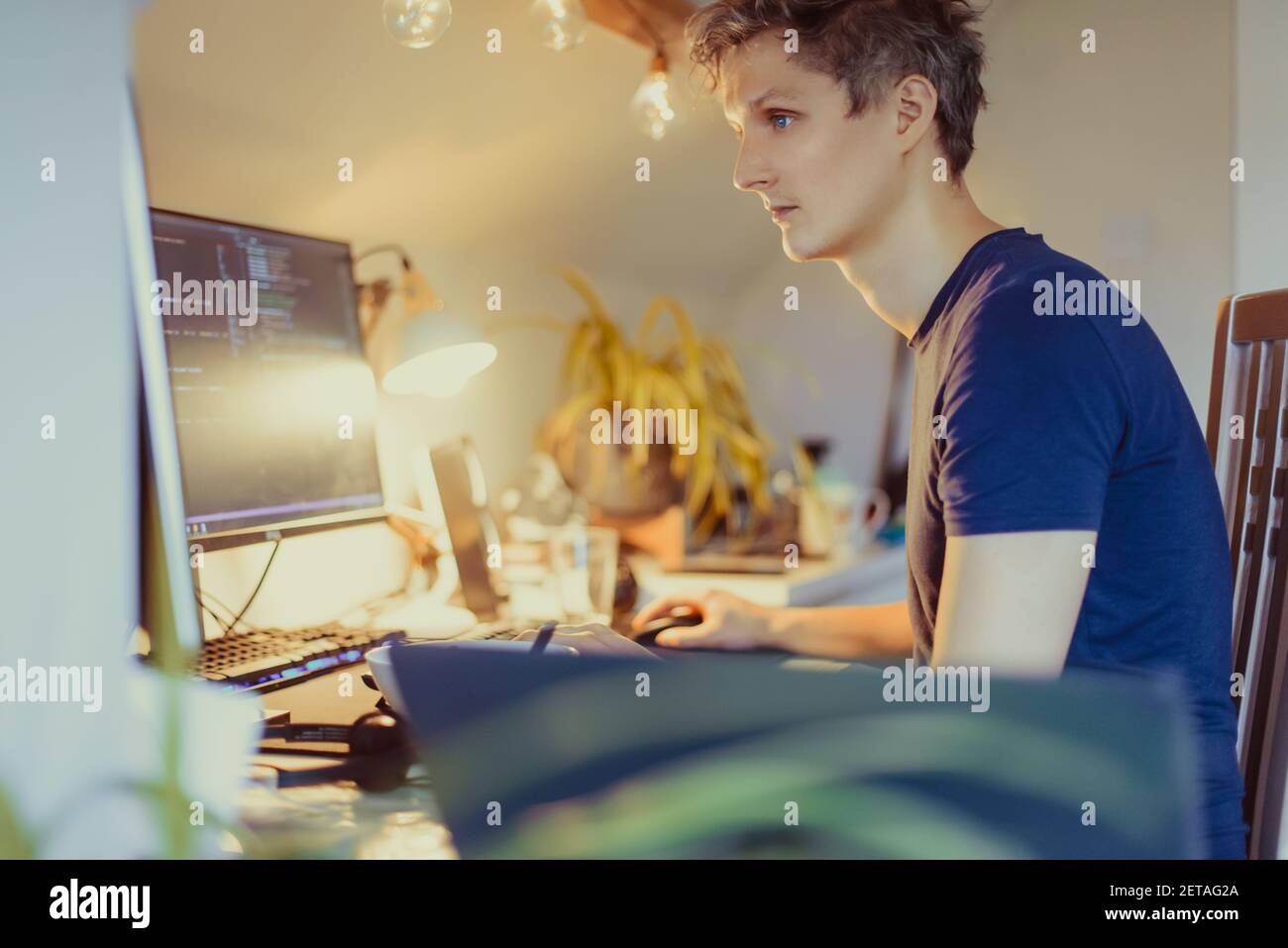 Ein Mann, der an einem Schreibtisch sitzt und von zu Hause aus an seinem Computer arbeitet. IT-Spezialist Programmierer schreiben Code auf seinem pc und Laptop. Entwickler Remote Home Office Stockfoto