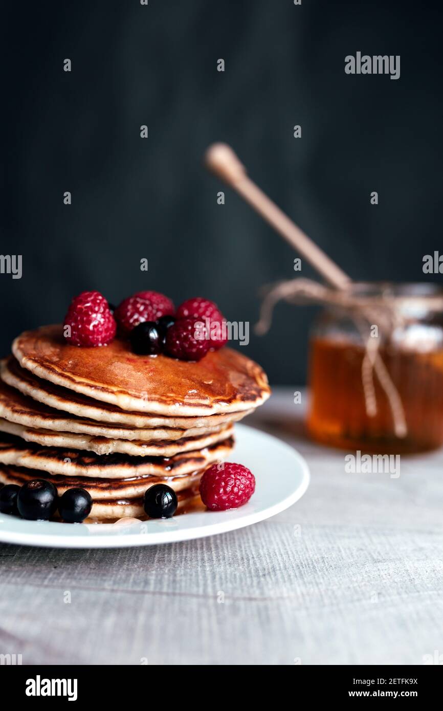 Saftige Pfannkuchen mit Beeren und Honig auf einem weißen Teller, Löffel, Glas, Holztisch. Hochwertige Fotos Stockfoto