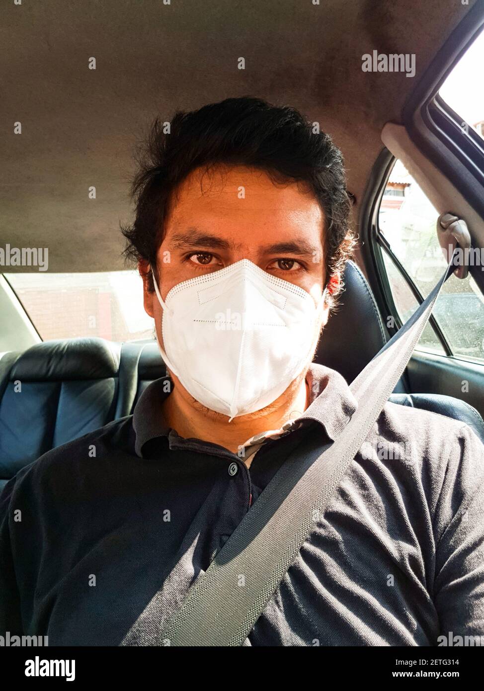 Ein Mann, der ein Auto fährt, legt während einer Epidemie eine medizinische Maske an, ein Taxifahrer in eine Maske, Schutz vor dem Virus. Fahrer im schwarzen Auto Stockfoto