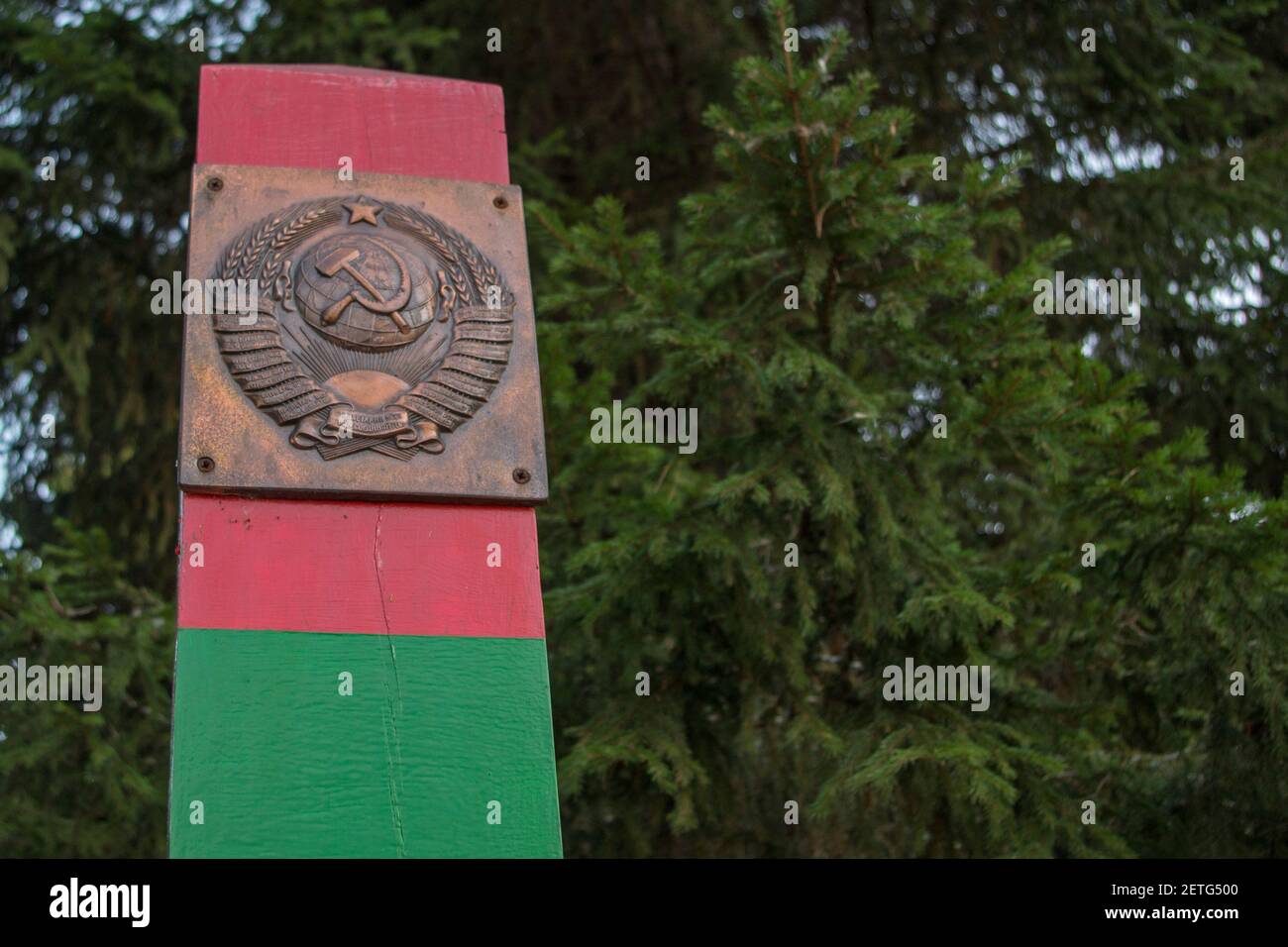 Die Oberseite des hölzernen Grenzpfosten in Grün und gemalt Rote horizontale Streifen mit einer Metallplatte, die das Fell darstellt Der Waffen der UdSSR, die in ihr befestigt sind Stockfoto