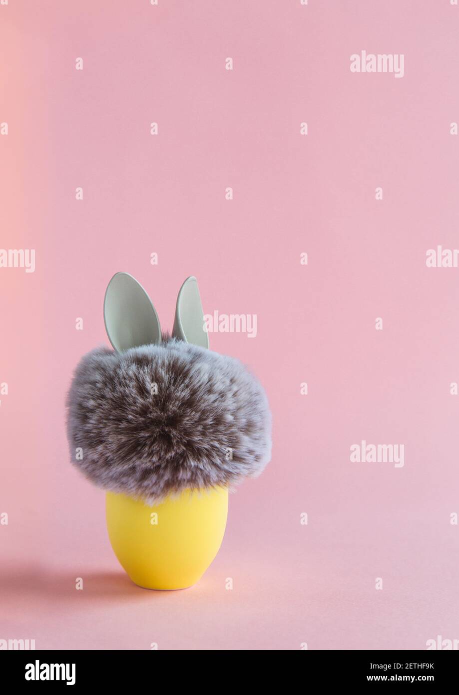 Pelzkugel mit Hase Kaninchenohren in gelbem Ei stehen auf hellem Hintergrund. Ostern Minimal Konzept. Nahaufnahme Stockfoto